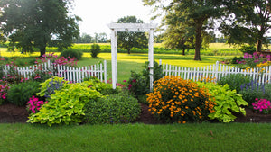 Large flower bed with flowers, arbor and fence.